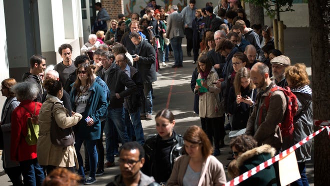 People line up before casting their vote for the first-round presidential election at a polling station in Paris on April 23, 2017.