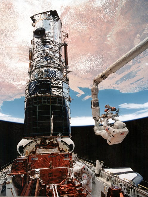 Astronaut F. Story Musgrave, anchored on the end of the Remote Manipulator System arm, prepares to be elevated to the top of the towering Hubble Space Telescope on Dec. 9, 1993, to install protective covers on magnetometers.