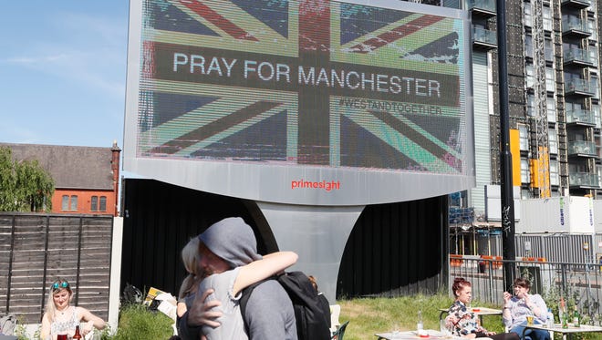 A couple embrace under a billboard in Manchester city centre, Tuesday May 23, 2017, the day after the suicide attack at an Ariana Grande concert that left 22 people dead as it ended on Monday night.