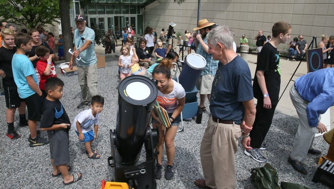 May Chee Yang (center) of Milwaukee takes a look at the eclipse through one of the telescopes available at the Milwaukee Public Museum's event. John Buntin, the telescope's owner and a volunteer (right), looks on, ready to assist.
