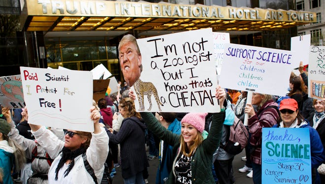 People hold signs in front of a Trump Hotel during a March for Science in New York.