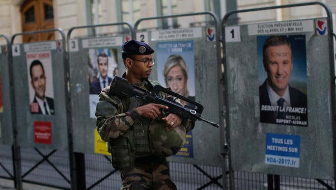 An army soldier patrols past posters showing faces of the candidates for the first-round presidential election near a polling station in Paris on April 23, 2017. French voters are casting ballots for their next president in an unusually close first-round election Sunday, after a campaign dominated by concerns about jobs and immigration and clouded by security fears following a recent attack on police guarding the Champs-Elysees in Paris.