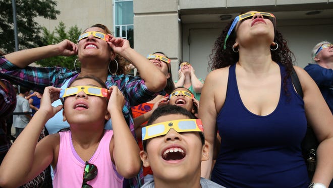 Mina Mares (upper left), Ilary Toro, 9 (lower left), James Mares, 8 (front center), and Amalia Baumann (right), all of Milwaukee, watch the eclipse with their eclipse glasses.