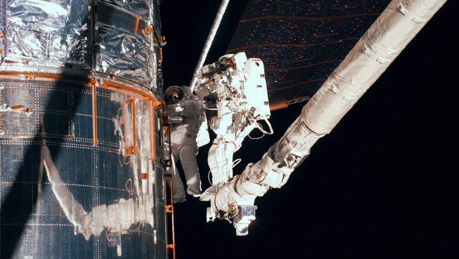 Making use of the remote manipulator system, astronauts Mark Lee, left, and Steven Smith repair the Hubble Space Telescope's peeling thermal insulation, the result of seven years of sun exposure, during space shuttle Discovery's servicing mission to the observatory on Feb. 18, 1997.