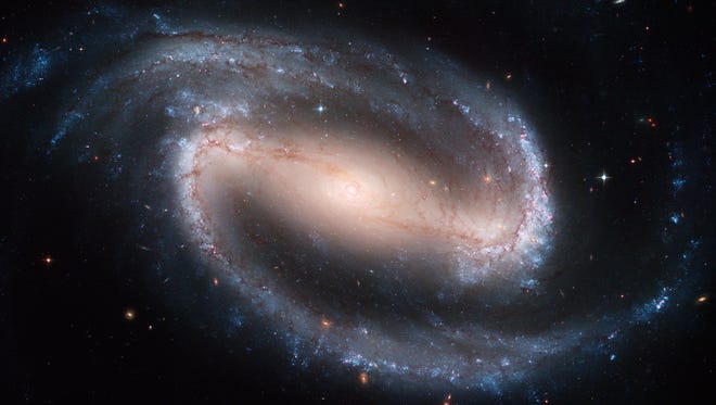 The Hubble telescope captured this display of starlight, glowing gas, and silhouetted dark clouds of interstellar dust of the barred spiral galaxy NGC 1300. Barred spirals differ from normal spiral galaxies in that the arms of the galaxy do not spiral all the way into the center, but are connected to the two ends of a straight bar of stars containing the nucleus at its center.